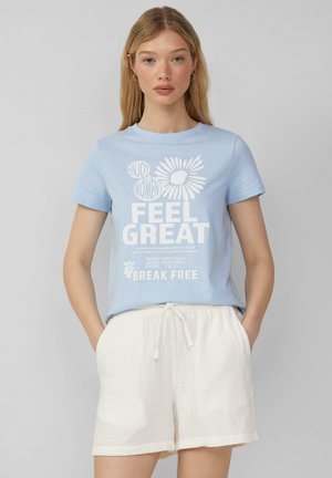 T-shirt en coton bleu clair avec un col rond, arborant un texte blanc et un graphique floral. Accompagné de shorts en lin de couleur crème.