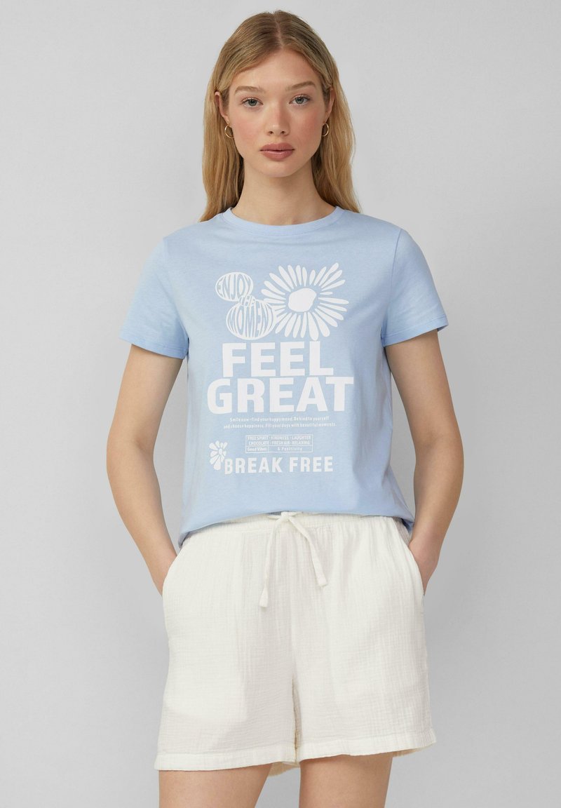 Lichtblauw katoenen T-shirt met een ronde hals, voorzien van witte tekst en een bloemig ontwerp. Gecombineerd met crèmekleurige linnen shorts.