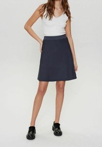 Tummanharmaa liehukehelmainen hame, jossa on sileä pinta ja leveä vyötärönauha, yhdistettynä valkoiseen ribbineulottuun toppiin ja mustiin massiivisiin kenkiin.