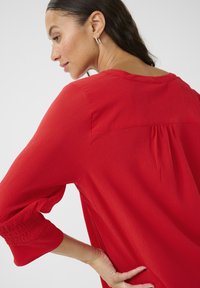 Rode blouse met een textuurafwerking, met 3/4 mouwen en een geraffineerd ontwerp aan de achterkant. Soepele stof en een relaxte pasvorm.