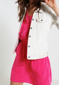 Vit denimjacka med silverknappar, kombinerad med en klar rosa klänning med samlad midja och rund halsringning.