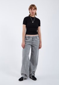 Zwarte top met korte mouwen en een getailleerd ontwerp, gecombineerd met hoge, wijde grijze jeans. Schoeisel is zwart sneakers. Eenvoudige sieradenaccenten.