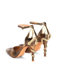 Zapatos de tacón alto de bronce metálico con punta puntiaguda, correas en el tobillo y acentos en forma de serpiente en los tacones. Textura suave con detalles en oro.