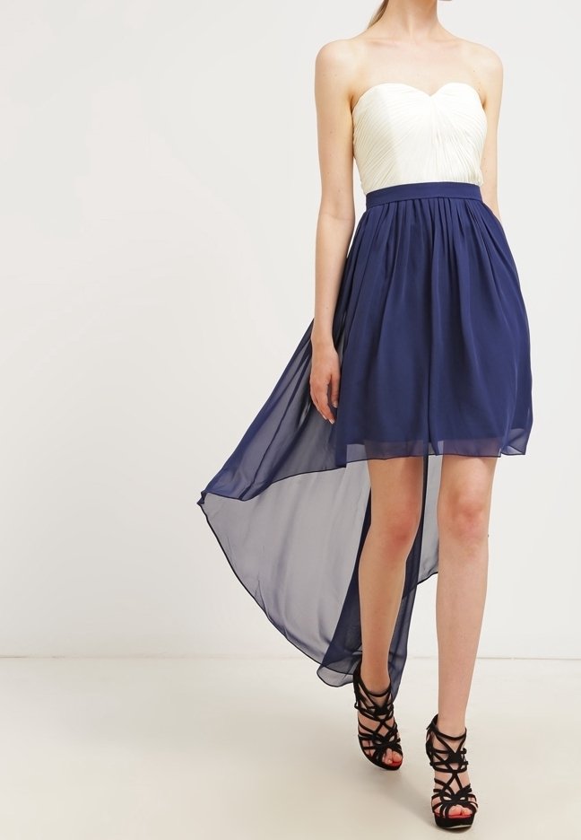 Sukienka bez ramiączek z białym koronkowym gorsetem i zwiewną granatową spódnicą z szyfonu, z wyższym przodem i niższym tyłem, zestawiona z czarnymi sandałami na obcasie.