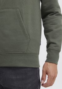 Oliven grøn sweatshirt med en lomme foran, ribbede manchetter og kant. Stofstrukturen ser blød ud, med synlige sømme og et lille mærke.