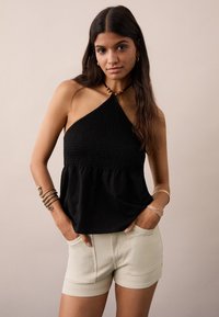 Čierny halter top so smotanovou spodnou časťou, párovaný s svetlými béžovými šortkami. Hladká tkanina a tesný strih.