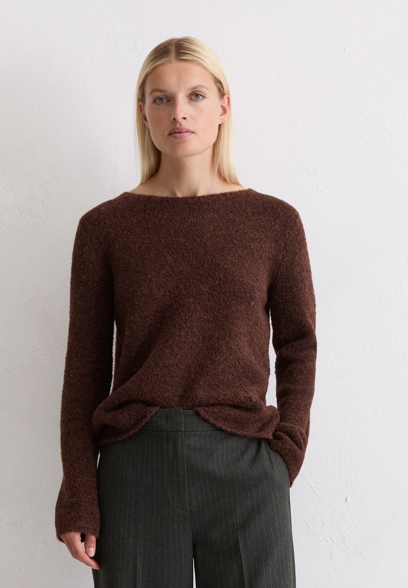 Pruun, tekstuuriga sviiter pikkade varrukatega ja laia kaelusega, kombinatsioon hallide triibuliste pükstega, kantud neutraalses taustas.