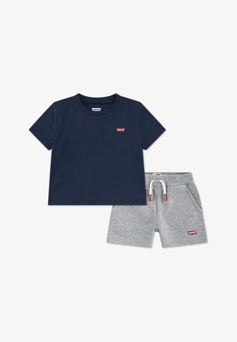 Marineblauw katoenen T-shirt met korte mouwen en een klein rood logo, gecombineerd met grijze katoenen shorts met een elastische tailleband en zakken.