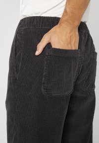 Pantalons en velours côtelé noir avec une texture côtelée, dotés de poches latérales et d'une taille élastique. Une vue en gros plan met en avant le détail des poches.
