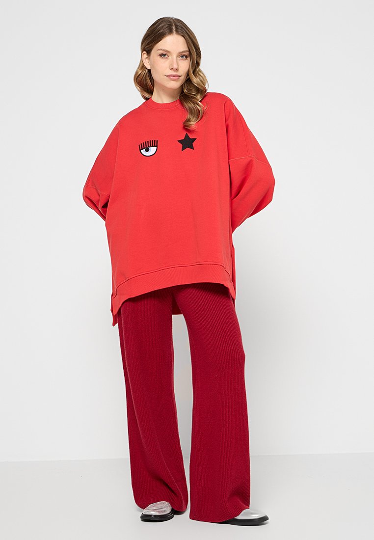 Czerwony oversize'owy sweatshirt z grafiką czarnego oka i gwiazd, zestawiony z czerwonymi, prążkowanymi spodniami o szerokich nogawkach. Gładki materiał i luźny krój.