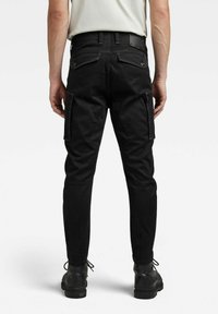 Svarte cargo-bukser med slim fit, med sidelommer og forsterkede sømmer. Stoffet har en glatt tekstur og er kombinert med svarte støvler.
