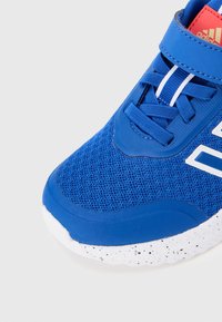 Μπλε αθλητικό παπούτσι με επάνω μέρος από δίχτυ, συμπαγείς λαστιχένιες επικαλύψεις, άσπρες λεπτομέρειες και υφή σόλας με μαύρες βούλες. Κλείσιμο με ρυθμιζόμενο λουρί.