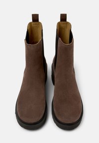 Botas de tobillo de ante marrón con punta redonda cerrada, suela de goma negra y doble tirador en la parte superior para facilitar su uso.