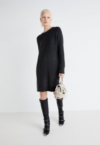 Robe en tricot côtelé gris foncé avec des manches longues, longueur mi-cuisse. Associée à des bottes noires à talons hauts ornées de clous et à bouts pointus.