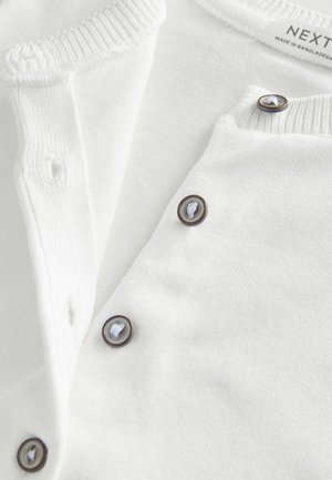 Weißer Cardigan mit einem gerippten Kragen, braunen Knöpfen mit weißen Fäden und einem weichen, strukturierten Stoff. Das Etikett trägt den Schriftzug "NEXT".