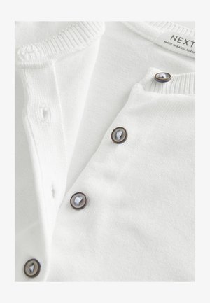 Cardigan alb cu guler tricotat cu nervuri, nasturi maro cu fire albe și un material moale și texturat. Eticheta spune "NEXT."