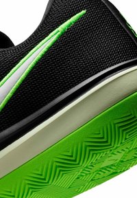 Κοντινό πλάνο μαύρου αθλητικού παπουτσιού με φλούο πράσινη σόλα, λευκή μεσαία σόλα και φλούο πράσινη κεντημένη ρίγα σε υφασμάτινη επιφάνεια με υφή.