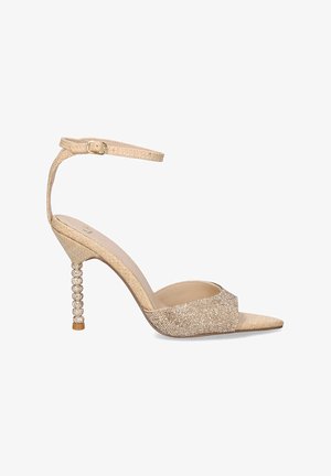 Sandalia de tacón de stiletto en color beige con tela texturizada, punta abierta y toques de purpurina. Cuenta con una correa de tobillo ajustable y un tacón con cuentas.