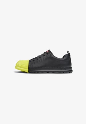 Sneaker in pelle nera con una punta in gomma gialla brillante. Caratterizzato da una superficie liscia, lacci rotondi e una suola in gomma nera.