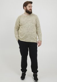 Pulover bej deschis cu un finisaj texturat și guler rotund, asortat cu pantaloni cargo negri care au buzunare laterale și adidași negri.