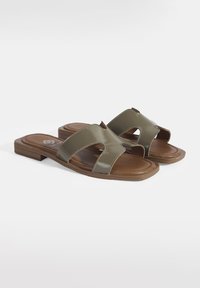 Sandales en olive vert avec un dessus en synthétique brillant, design à bout ouvert et semelle plate marron. Caractéristiques de deux bride se chevauchant avec des détails de couture.