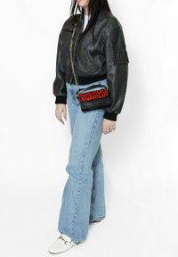 Giacca bomber nera in pelle con polsini a coste, jeans a zampa d'elefante blu chiaro e una piccola borsa a tracolla nera e arancione con stampa leopardata.