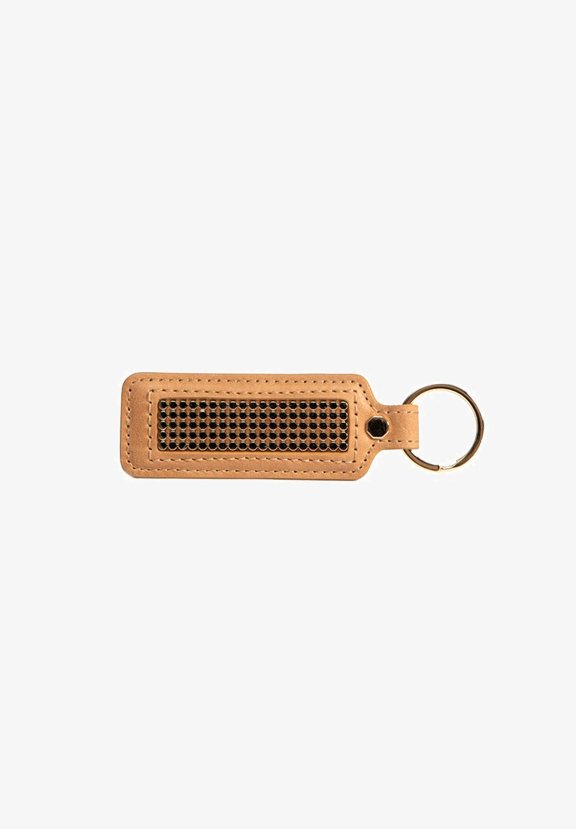 Porte-clés en cuir beige avec un détail en maille noire texturée. Comprend un anneau en métal circulaire pour l'attachement.