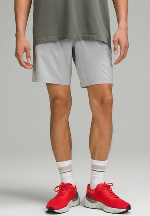 Shorts atletici grigio chiaro in tessuto intrecciato, con una texture liscia e un design semplice. Indossati con scarpe rosse e calzini a righe bianche.