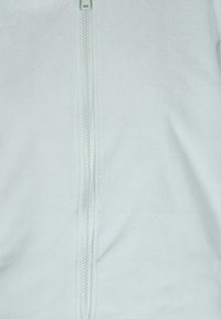 Giacca in pile azzurro chiaro con texture liscia e una cerniera argentata che scende al centro, senza ulteriori motivi o dettagli.