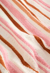 Tissu doux avec des rayures texturées ondulées en rose, blanc et marron, plié et superposé, mettant en valeur un motif textile confortable et chaleureux.