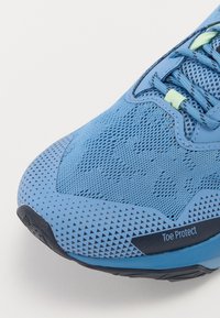 Zapatilla deportiva azul con parte superior de malla transpirable, superficie texturizada y capuchón protector con etiqueta "Toe Protect". Suela de goma con tracción.