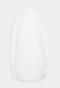 Vit oversized cardigan med ett strukturerat stickat mönster, hög krage och sidoklyftor för bättre rörelsefrihet. Design utan knäppning.