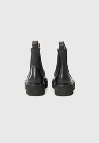 Bottines en cuir noir avec une texture lisse, semelles en caoutchouc épaisses et poignées à l'arrière. Présente un design élégant et épuré.