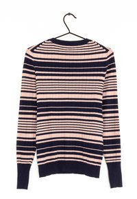 Sweter w paski z długim rękawem w kolorach różowym i granatowym, z prążkowaną teksturą i okrągłym dekoltem. Zawieszony na czarnym haczyku.