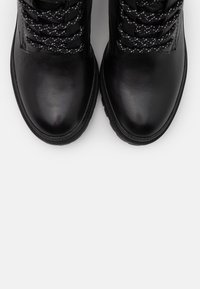 Czarne skórzane botki na kostkę z okrągłymi noskami, sznurowane z przodu, z kontrastującymi białymi i czarnymi sznurowadłami, teksturowana powierzchnia i gumowa podeszwa.