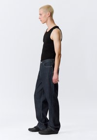 Μαύρο αμάνικο τοπ σε συνδυασμό με φαρδιά, σκουρόχρωμα μπλε τζιν. Διαθέτει ραφές με επένδυση και κουμπιά για κλείσιμο. Μαύρα παπούτσια ολοκληρώνουν την εμφάνιση.