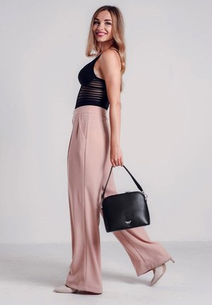 Schwarze Ledertasche mit strukturierter Form, getragen von einer Person in einem schwarzen Oberteil und hellrosa hoch taillierten Hosen. Texturiertes Design auf der Oberseite.