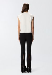 Top blanco de manga corta con un corte relajado, combinado con pantalones ajustados negros con slit laterales y zapatos de tacón alto negros.