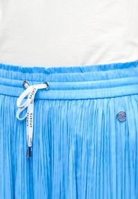 Μπλε πλισέ φούστα με ελαστική μέση και λευκό κορδόνι με την επιγραφή "SPORTS", σε συνδυασμό με λευκό τοπ.