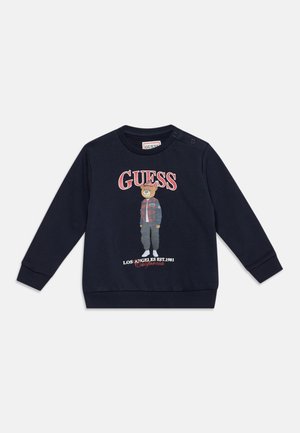 Sweat-shirt bleu marine à manches longues pour tout-petits avec un ours portant des vêtements décontractés et le texte "GUESS Los Angeles EST. 1981 California" à l'avant.
