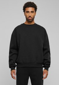 Felpa nera con collo rotondo, vestibilità ampia e polsini e orlo ribattuti. Realizzata in un tessuto morbido e testurizzato, con uno stile minimalista.