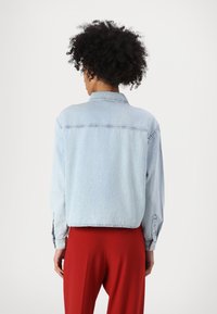 Ljusblå denimjacka med krage, knappade manschetter och croppad passform, matchad med röda byxor. Slät textur och avslappnad design.