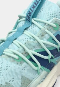 Chaussure de sport bleu clair avec dessus en mesh, accents texturés et lacets réglables. Dispose d'une semelle multicolore à motifs et d'une étiquette de marque.