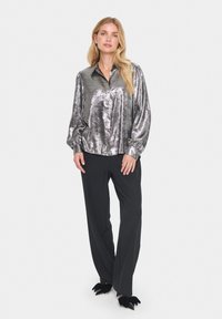 Silver metallic button-up shirt with long sleeves, paired with black trousers and black shoes featuring bow accents.