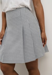 Jupe en plaid noir et blanc avec un design évasé, des plis, une texture de tissu lisse et une taille cintrée. Gros plan montrant le placement de la main.