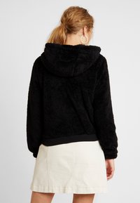 Czarna polarowa bluza z kapturem o miękkiej fakturze, z ribbowanym wykończeniem. Noszona z jasną spódnicą, podkreślająca design bluzy.
