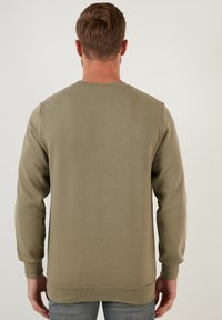 Sudadera verde oliva con una superficie texturizada, cuello redondo y mangas largas. Cuenta con puños y dobladillo acanalados, diseño minimalista.