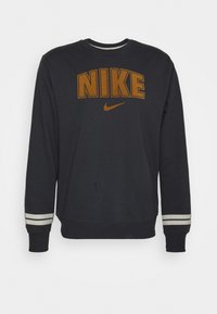 Sudadera negra con gran logotipo naranja de "NIKE", cuello redondo y detalles a rayas grises en los puños. Tejido de algodón, corte relajado.