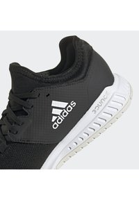 Chaussure de sport Adidas noire avec logo "adidas" blanc et semelle coussinée blanche avec marquage "bounce", vue de côté et de dos.