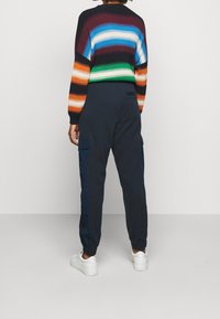 Randig stickad tröja med flerfärgade horisontella linjer, ihop med marinblå cargobyxor med sidofickor och elastiska mudd, bärs med vita skor.